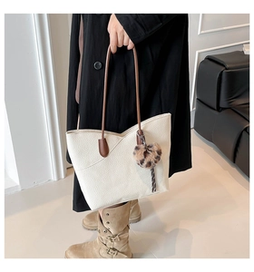 Detailed view of white lychee leather tote with brown handles and leopard plush charm