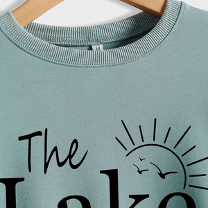 Blue-green crewneck sweatshirt with 'The Lake' print on a wooden hanger view