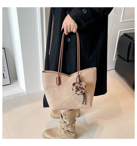 Detail of khaki leather tote bag with brown handles and a leopard heart plush charm