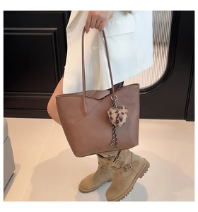 Detail of brown lychee grain leather tote bag with a leopard heart charm on a white blazer