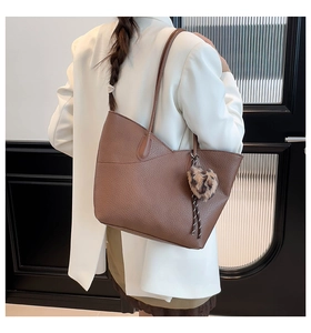 Detail of dark brown pebble leather tote bag with wavy top edge and leopard pom-pom charm