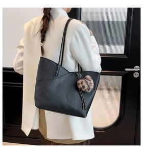 Detail of black pebbled tote bag with elegant wavy edge and leopard fur ball charm