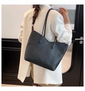 Detail of a large black lychee texture leather tote bag worn by a model in a work setting