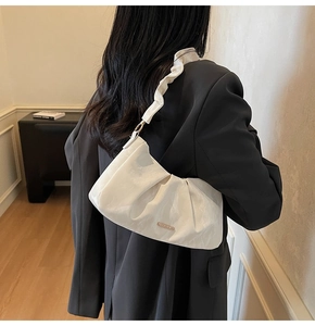 Dettaglio della borsa a nuvola bianca plissettata con logo in metallo su una modella