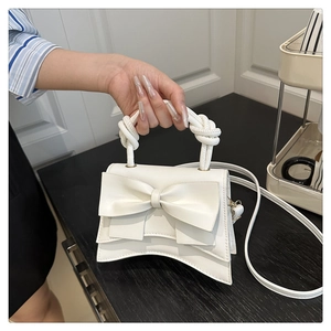 Detail of white faux leather crossbody bag with knot handle and 3D bow decoration