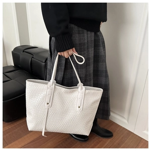 Close-up of white woven tote bag with dual straps held by model in casual outfit
