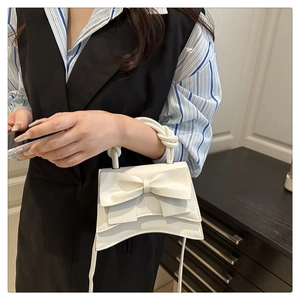 Detail of white bow handbag with knotted handle and elegant wave bottom design