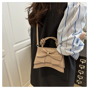 Detail of beige bow crossbody bag showing textured fabric and twisted rope handle
