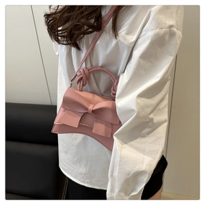 Détail du sac à main rose avec nœud, poignée torsadée et bandoulière porté par un mannequin