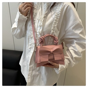 Detailed shot of pink bow crossbody bag with twisted top handle and matching shoulder strap