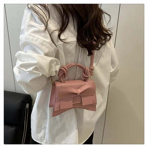 Pink mini crossbody bag with a large bow detail and braided top handle shown on a model