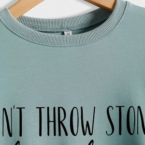 Sweatshirt vert clair avec imprimé DON'T THROW STONES sur un cintre en bois
