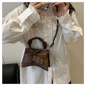 Detailed view of the dark brown hourglass handbag featuring a large decorative bow