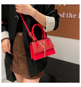 Detail of red leather crossbody bag featuring a golden V hardware and stylish silk tassel