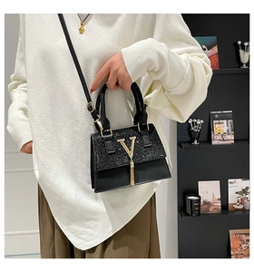 Close-up of black handbag featuring a gold V-logo, tassel detail and matte sequin texture