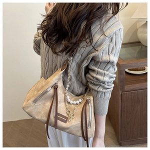 Détail du sac à bandoulière kaki avec chaîne, perles et trèfle porté sur un pull marron