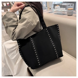 Détail d'un sac cabas noir avec des rivets argentés sur le côté et la bandoulière