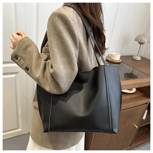 Close-up of a large black leather tote bag with dual straps worn over a khaki blazer