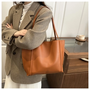 Side view of large orange-brown tote bag with fine leather texture on model's shoulder