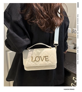 Detail of white quilted crossbody bag featuring gold LOVE hardware and a wide strap