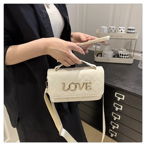 Detail of cream quilted crossbody bag with gold LOVE emblem and wide fabric strap
