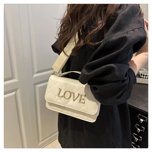 Close-up of quilted cream crossbody bag with gold LOVE metal lettering and wide strap