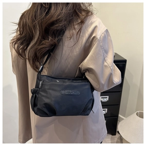 Detail of minimalist black nylon shoulder bag with pleated sides and brand labels