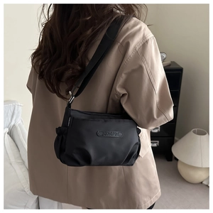 Detail of a black nylon crossbody bag with pleated sides worn in a cozy home setting