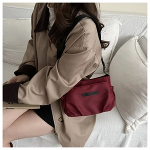 Detail view of burgundy nylon pleated crossbody bag worn by a model in casual setting