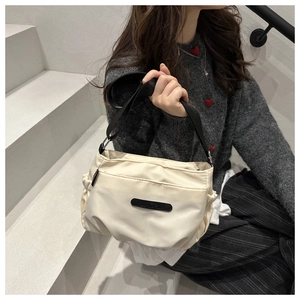 Detail of minimalist cream nylon shoulder bag with pleated design and black strap