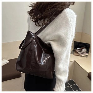 Detail of glossy brown patent leather tote bag showing mirror-like shine and silver rivets