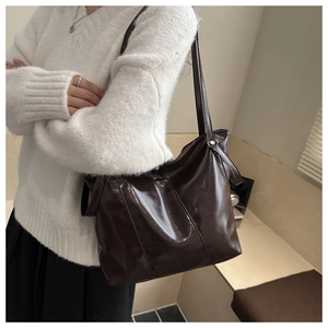 Detail view of large dark brown glossy leather tote bag worn over the shoulder by a model