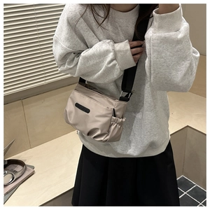 Detail of beige nylon crossbody bag with wide black strap and elastic side pocket