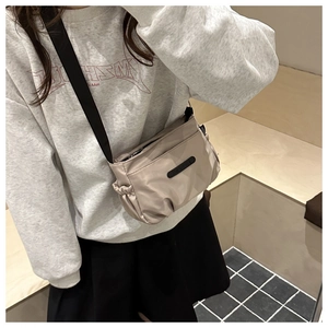 Detail of light khaki nylon crossbody bag with black rubber logo and adjustable strap