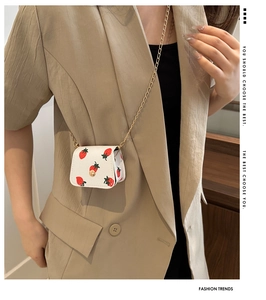 Mini portefeuille blanc à motif fraise avec chaîne dorée porté sur un blazer beige