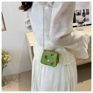 Mini sac vert à motif fraise porté en bandoulière avec une fine chaîne dorée