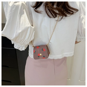 Détail du mini sac bandoulière à imprimé fraise avec chaîne dorée porté par un mannequin