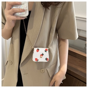Gros plan du mini sac blanc à motif fraise avec chaîne dorée sur une tenue chic