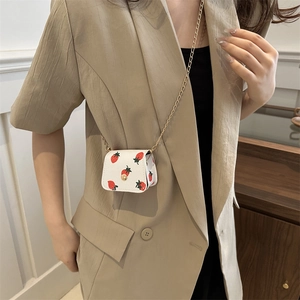 Mini sac bandoulière blanc avec motif fraise et chaîne dorée porté par un mannequin