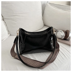 Close-up of black patent leather crossbody bag with dual straps on white fabric sofa
