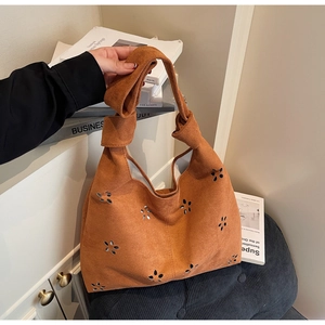 Détail du sac cabas en daim caramel avec fleurs ajourées et poignée nouée sur un canapé