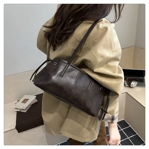 Detail of dark brown leather tote bag showing the side drawstring knot and long handles