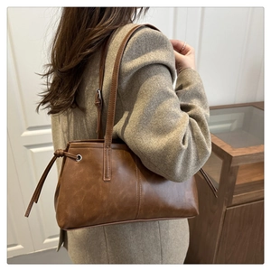 Close-up of caramel brown leather tote bag showing side drawstring detail and long straps