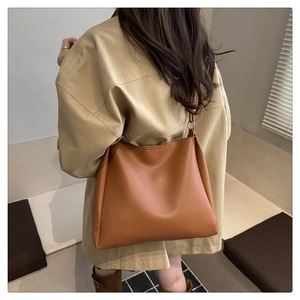 Detailed side view of a large caramel leather tote bag worn on shoulder by a model