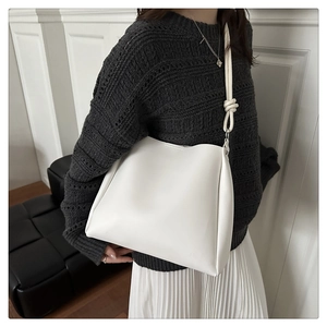 Detail of white leather shoulder bag with decorative strap knot on grey knit sweater