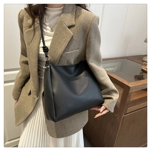 Detail of a large black vintage shoulder bag worn by a model in a brown suit