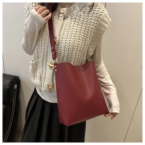 Close-up of deep burgundy leather bucket bag with wide strap and gold metal rivets