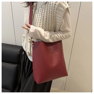 Minimalist red leather bucket bag with gold stud detail and wide shoulder strap