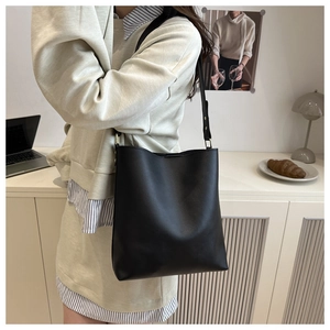 Minimalist black PU leather bucket bag with slim shoulder strap in a cozy interior setting