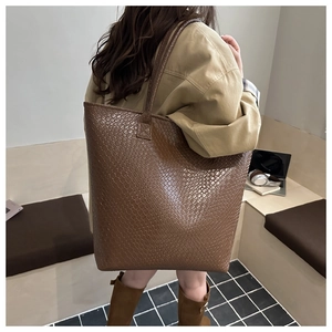 Detail of a large brown woven tote bag showing texture and shoulder strap fit on a model